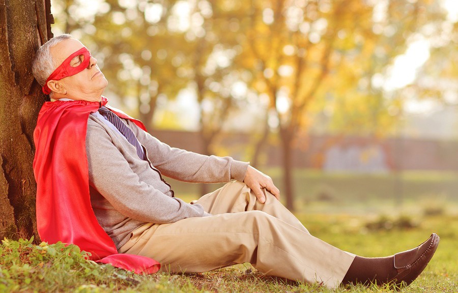 Senior in superhero outfit leaning on tree in park